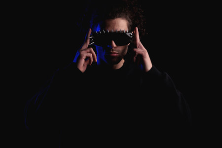 confident mysterious man with curly hair adjusting cool sunglasses in front of black background in studioの写真素材