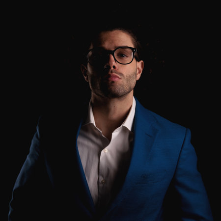 portrait of elegant young businessman with glasses confidently posing in front of black background in studioの写真素材