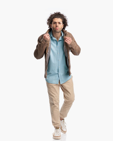 full body picture of attractive man with curly hair and glasses adjusting jacket and stepping in front of white background in studioの写真素材