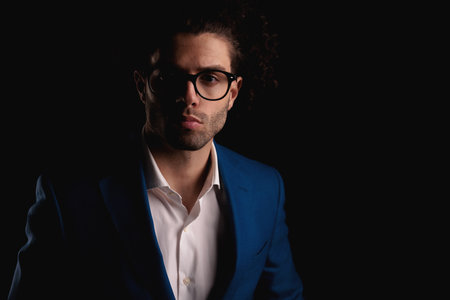 portrait of handsome businessman with glasses wearing blue suit and glasses with open collar shirt posing in front of black backgroundの写真素材
