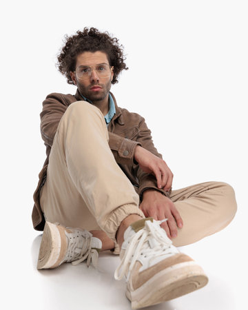 sexy fashion man with curly hair and glasses sitting on the floor in front of white backgroundの写真素材