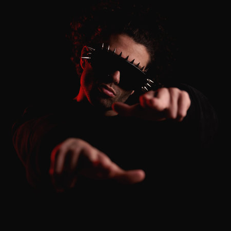 cool fashion man with glasses pointing fingers forward in a confident way in front of black background with red lights onの写真素材