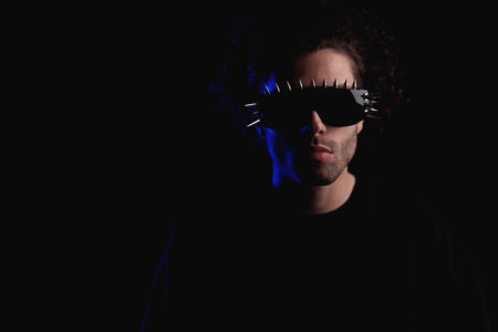 portrait of young casual man with curly hair wearing cool sunglasses and posing in front of black backgroundの写真素材