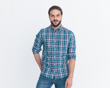 sexy unshaved man wearing casual plaid shirt holding hands in pockets and posing in a cool way on grey backgroundの写真素材