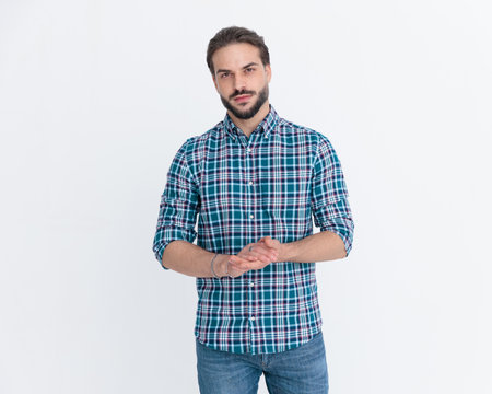 handsome casual man with beard in plaid shirt rubbing palms and posing in a confident way in front of grey backgroundの写真素材