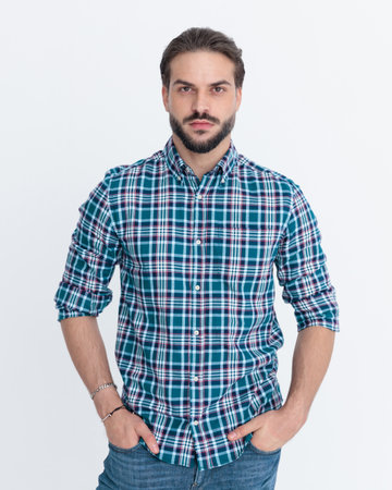 bearded man in casual plaid shirt holding hands in pockets, standing and posing in front of grey backgroundの写真素材