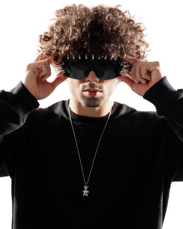 attractive young man with curly hair holding and adjusting cool sunglasses in front of white backgroundの写真素材