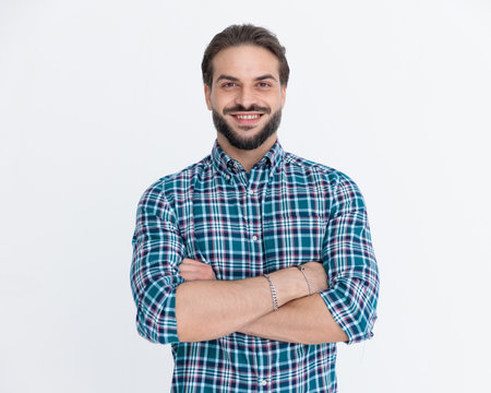 portrait of happy casual man in plaid shirt crossing arms and smiling in front of grey backgroundの写真素材