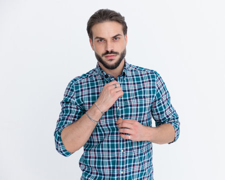 sexy young man with beard unbuttoning casual plaid shirt, looking forward and posing in front of yellow backgroundの写真素材