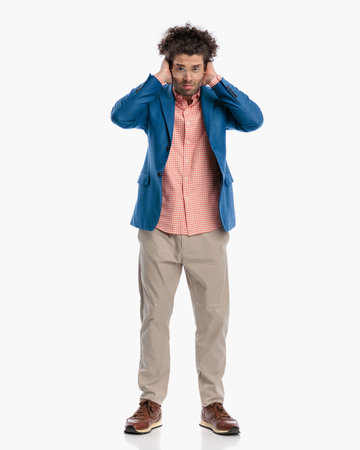 full body picture of attractive young man with glasses covering ears and trying not to hear while standing in front of white background in studioの写真素材