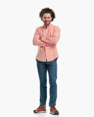 full body picture of smart casual man with curly hair and glasses smiling and crossing arms while standing in front of white backgroundの写真素材
