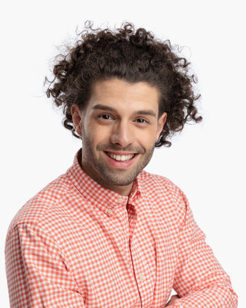 handsome man with curly hair smiling and crossing arms in front of white background in studioの写真素材