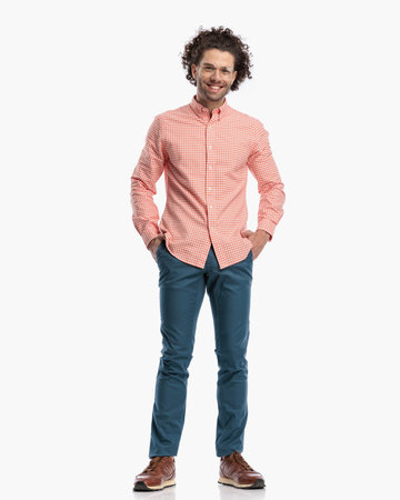curly hair guy with glasses holding hands in pockets, being happy and smiling in front of white background in studioの写真素材