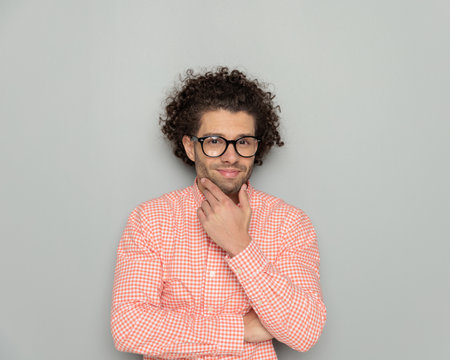 portrait of confident man with glasses wearing plaid shirt touching chin and wondering while posing in front of grey backgroundの写真素材