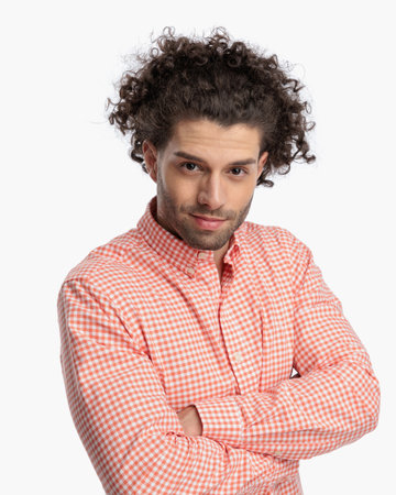 portrait of sexy young man with curly hair in plaid shirt crossing arms and smiling in front of white background in studioの写真素材