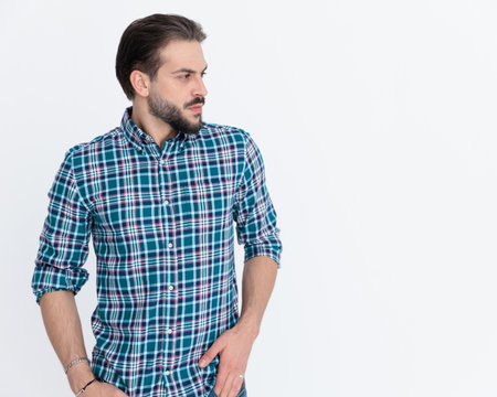 young casual man in plaid shirt holding hands in pockets and looking to side in fronf of grey backgroundの写真素材