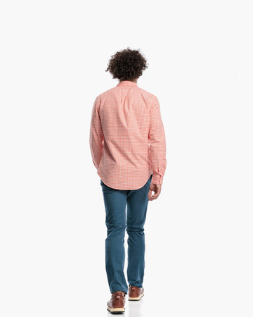back view of casual man with curly hair in plaid shirt and sneakers walking in front of white background in studioの写真素材