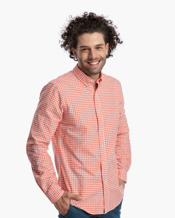portrait of happy man in plaid shirt with curly hair smiling and holding hands in front of white background in studioの写真素材
