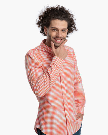 handsome casual guy with curly hair touching chin and wondering while posing with hand in pocket and smiling on white backgroundの写真素材