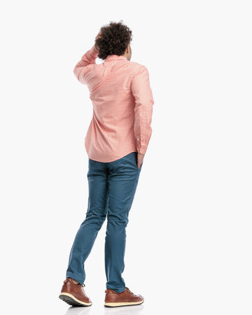 thoughtful young man with curly hair walking with hand in pocket while scratching head and thinking in front of white background in studioの写真素材