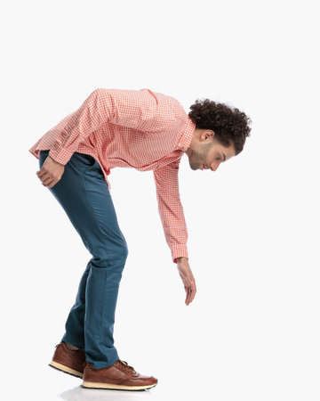 side view of casual man with curly hair leaning forward while walking and looking down in front of white background in studioの写真素材