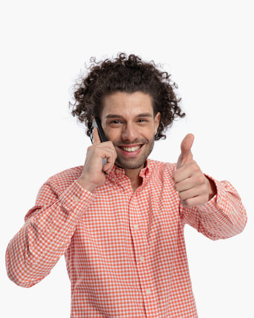 happy young man having a phone conversation and making thumbs up gesture in front of white backgroundの写真素材