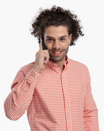 portrait of sexy young man with curly hair smiling and talking on the phone in front of white background in studioの写真素材