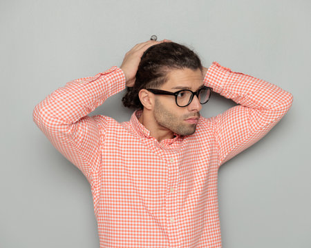 sexy young man with glasses running fingers through hair and looking to side while adjusting hair in front of grey backgroundの写真素材