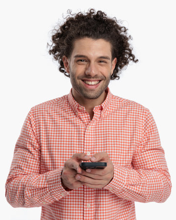 happy casual man with curly hair laughing while texting messages in front of white backgroundの写真素材