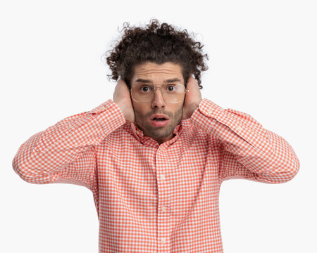 scared young man with glasses covering ears and trying not to hear loud noises in front of white backgroundの写真素材