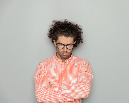 portrait of upset young man with glasses crossing arms and frowning in front of grey backgroundの写真素材