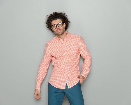 sexy curly hair man with glasses posing in a cool way with hand in pocket in front of grey backgroundの写真素材