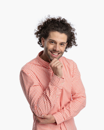 happy young guy with curly hair touhing chin and thinking in front of white background in studioの写真素材