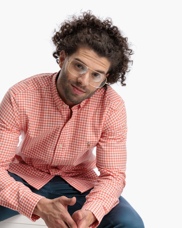 cutout picture of handsome curly hair man with glasses smiling while rubbing palms and sitting in front of white background in studioの写真素材