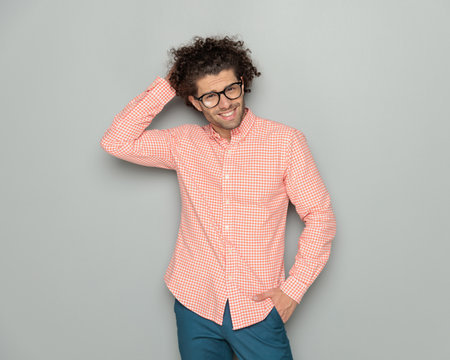 handsome casual guy with glasses holding hand to hair and fixing it while posing with hand in pocket on grey backgroundの写真素材