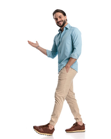side view of young man walking with hand in pocket and welcoming in front of white backgroundの写真素材