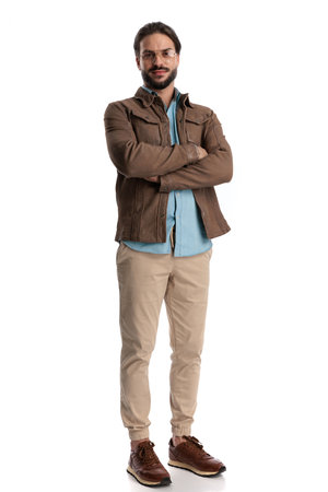 happy bearded man with glasses smiling and crossing arms while standing and posing in front of white backgroundの写真素材