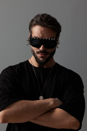 attractive cool guy wearing sunglasses and crossing arms in front of dark grey background in studioの写真素材