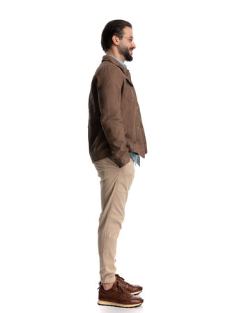 side view of smiling young man looking to side and waiting with hands in pockets in front of white backgroundの写真素材