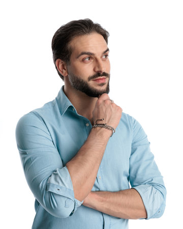 pensive casual man touching chin, looking away and dreaming while folding arms in front of white backgroundの写真素材