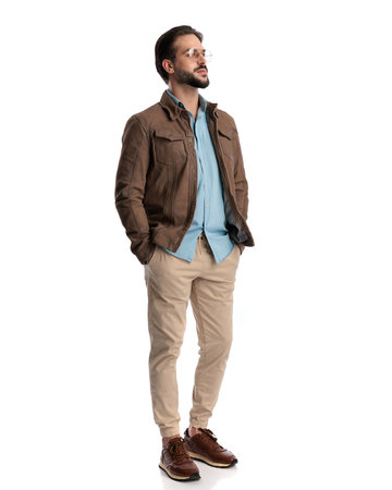 sexy bearded man with glasses holding hands in pockets and looking to side in front of white backgroundの写真素材