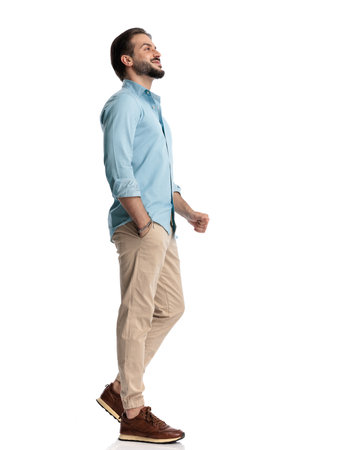 side view of happy casual guy walking with hand in pocket and smiling in front of white backgroundの写真素材