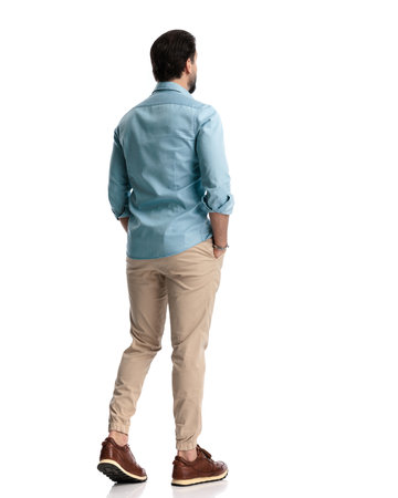 behind view of casual man in denim shirt walking with hands in pockets in front of white backgroundの写真素材
