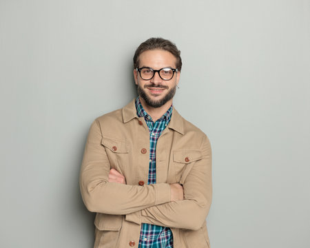 handsoe happy man with glasses smiling while crossing arms and posing in front of grey backgroundの写真素材