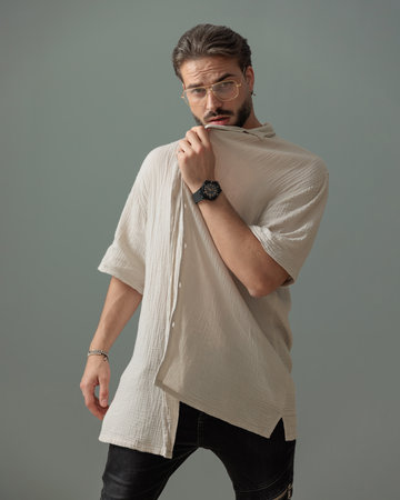 sexy young man with glasses pulling and covering face with shirt while posing in front of grey backgroundの写真素材