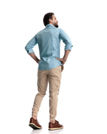 rear view of casual young man looking away and walking in front of white backgroundの写真素材
