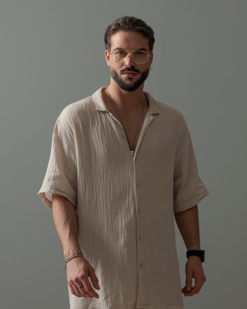 attractive bearded man with glasses looking forward and confidently posing in front of grey backgroundの写真素材