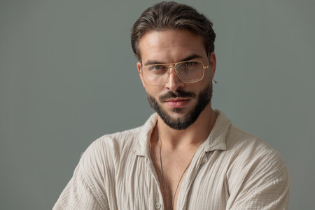 portrait of sexy bearded guy with glasses looking forward and posing in front of grey backgroundの写真素材