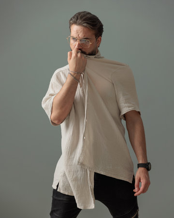 fashion guy with glasses looking away while covering face with shirt in front of grey backgroundの写真素材