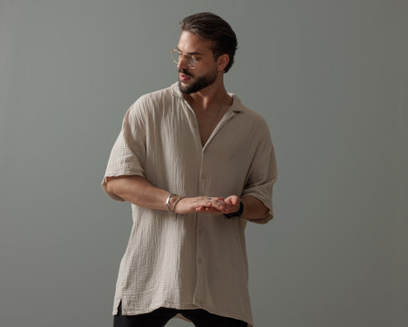 sexy fashion guy with glasses rubbing palms and looking to side in front of grey backgroundの写真素材